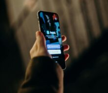 Close-up of a hand holding a smartphone displaying a login interface. Blurred background.