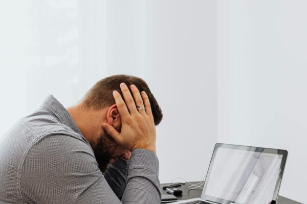 A frustrated man sits at a desk with a laptop and charts, showing work stress.